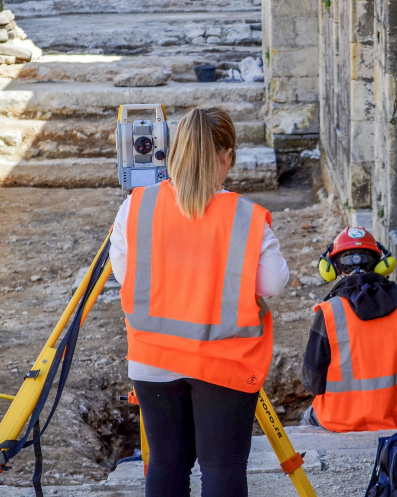 Two ground engineers in personal protective clothing use surveying instruments to assess a construction site